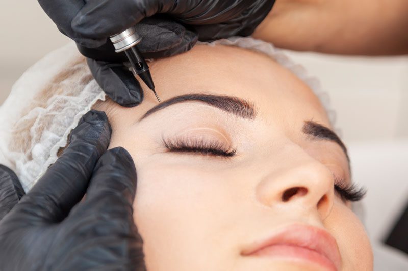 A woman getting her eyebrows tattooed with black ink.